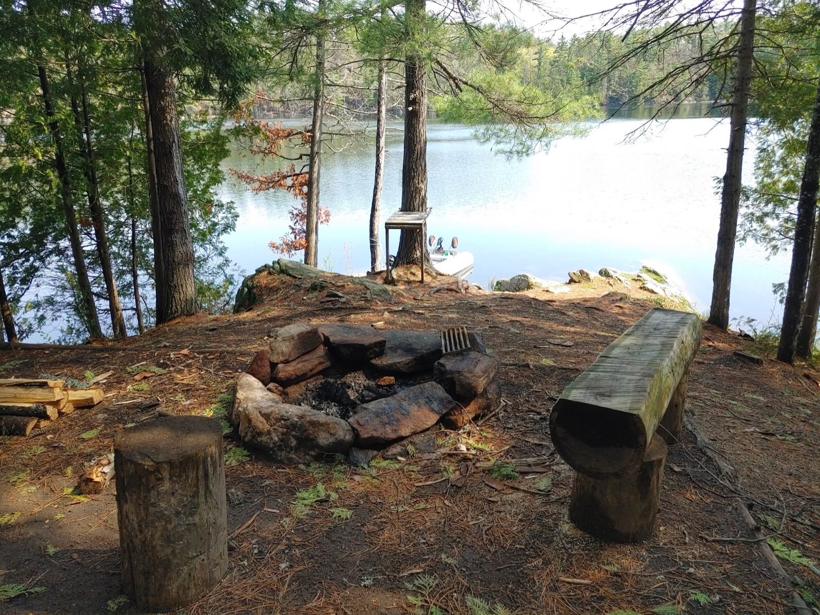 Stone fire pit and split-log bench at a Wabun Lake Crown Land campsite framed by pines